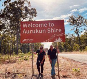 Two case managers in uniform in front of a directional sign to heading into Aurukun Shire